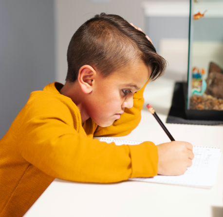 A young boy with Achondroplasia sitting at a table doing homework